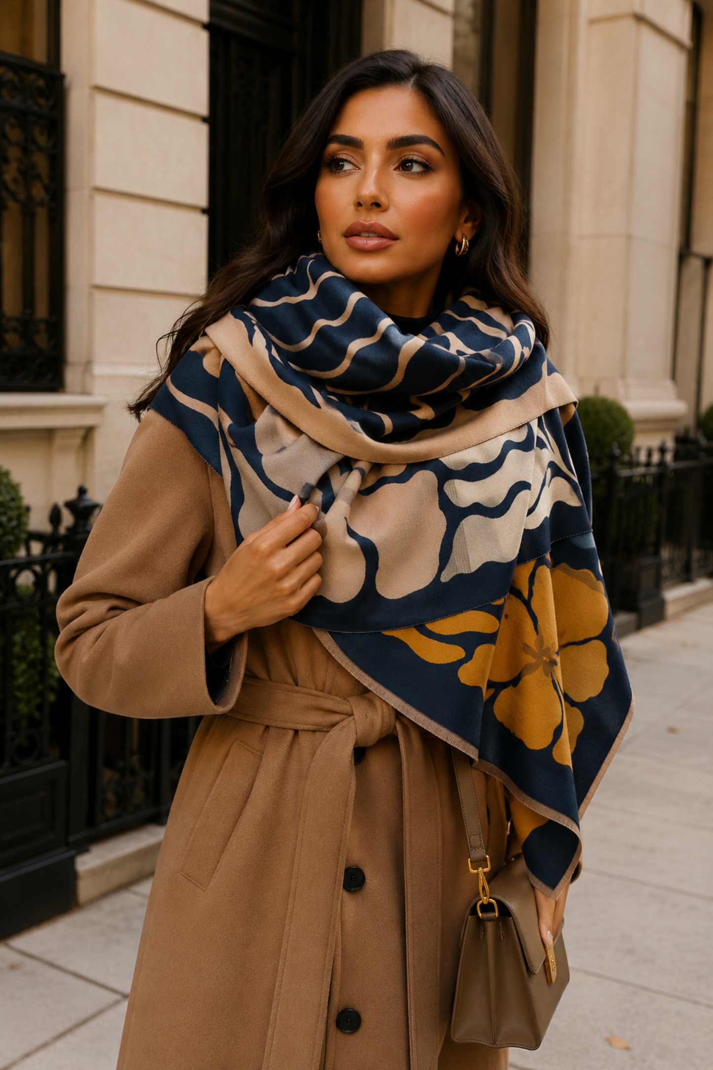Woman wearing a patterned scarf and beige coat on a city street.