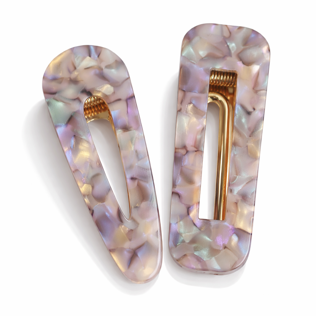 Two decorative hair clips with a shell pattern and gold accents on a white background