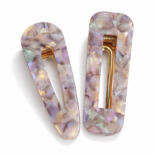 Two decorative hair clips with a shell pattern and gold accents on a white background