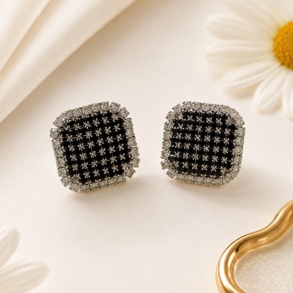 Black square earrings with diamond-like stones on a light background with daisies.