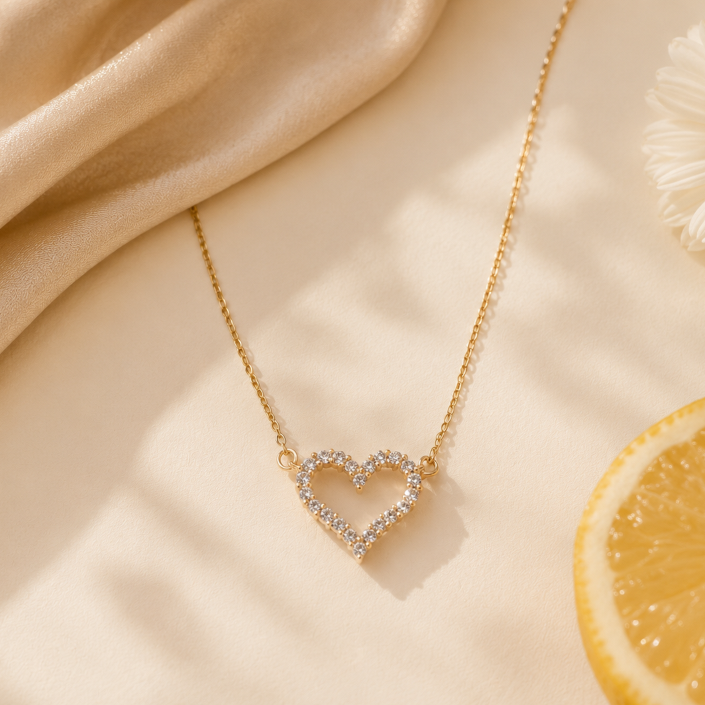 Gold necklace with a heart pendant on a beige fabric background with a lemon and flower.
