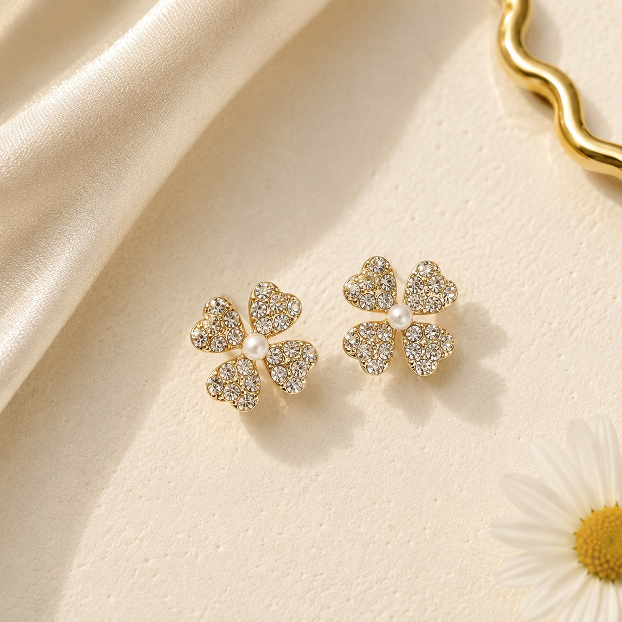 Gold four-leaf clover earrings with pearls on a beige fabric background