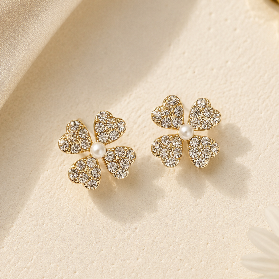 Gold four-leaf clover earrings with pearls on a beige fabric background