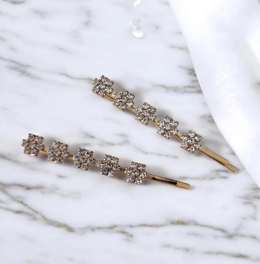 Two gold hair pins with crystal stones on a marble surface