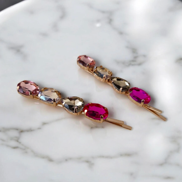 Pair of gold hair pins with multicolored gemstones on a marble surface