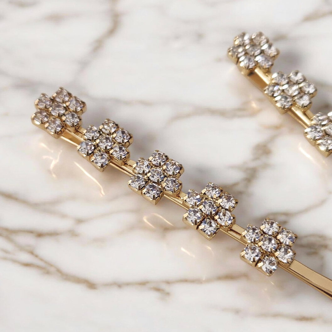 Gold hair pins with crystal-like stones on a marble background