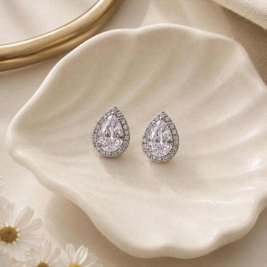 Teardrop-shaped earrings on a white ceramic dish with a soft beige background
