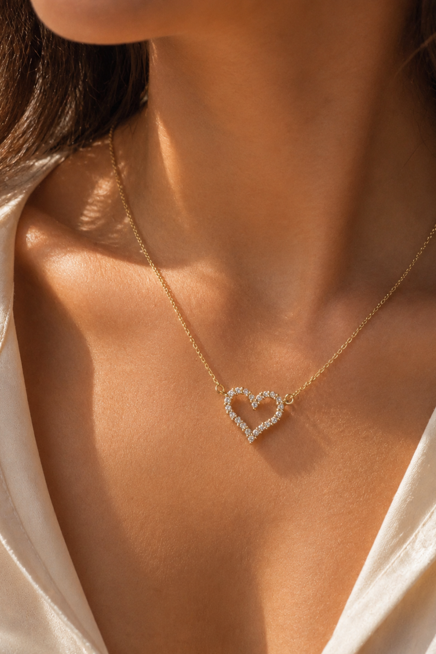 Gold necklace with a heart-shaped pendant on a person wearing a white shirt.