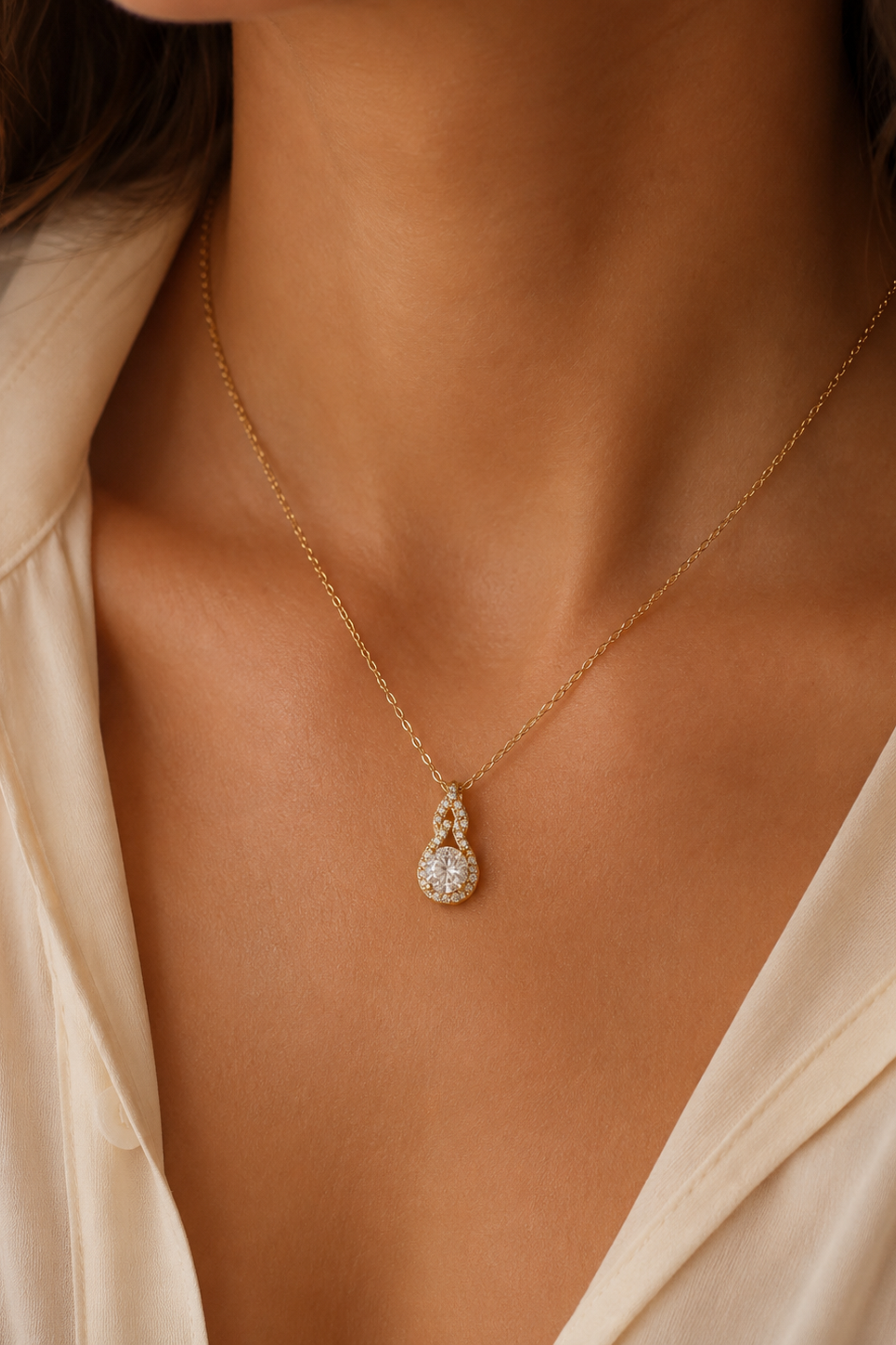 Gold necklace with a diamond pendant on a person wearing a beige top.