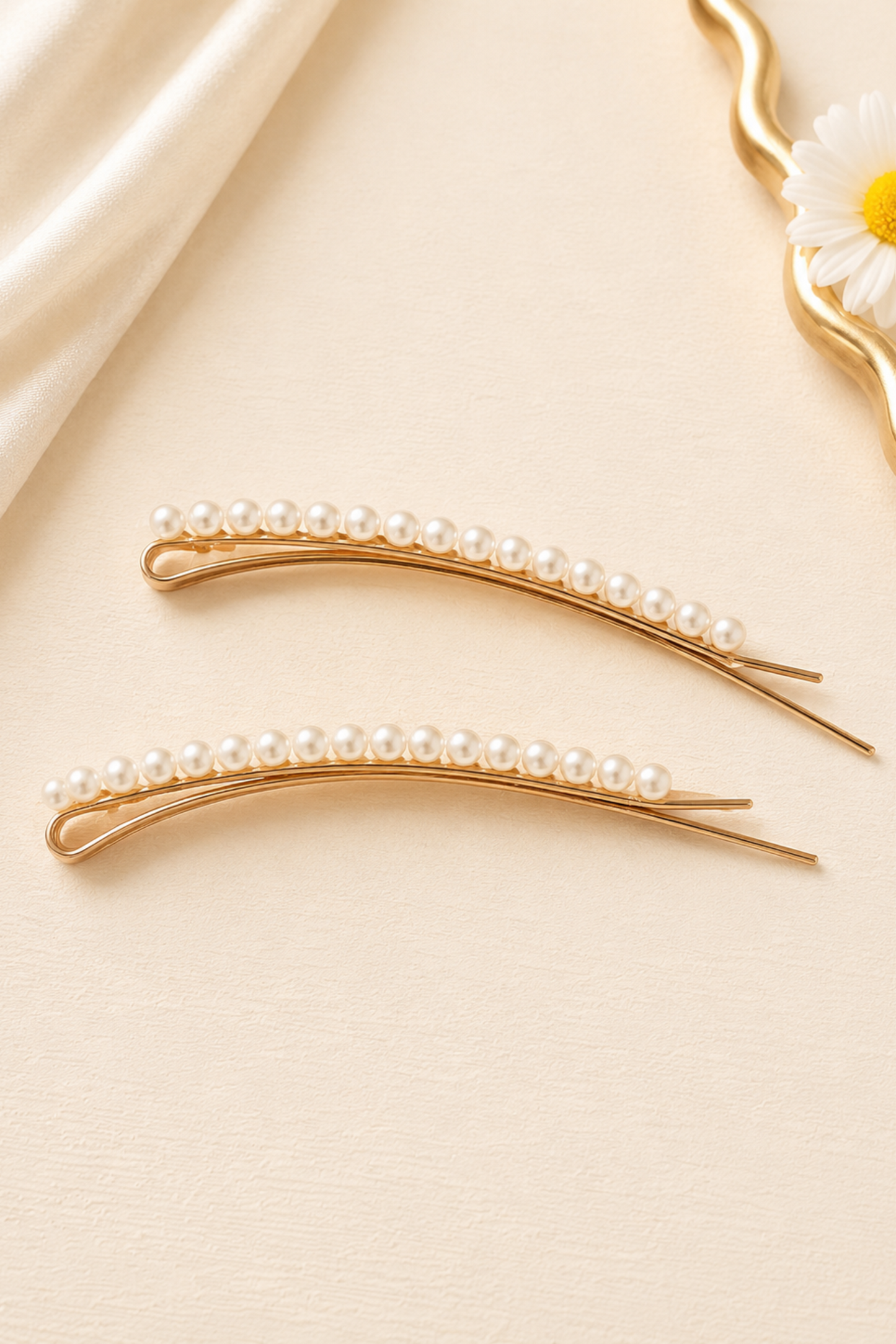 Two gold hairpins with pearls on a beige fabric background