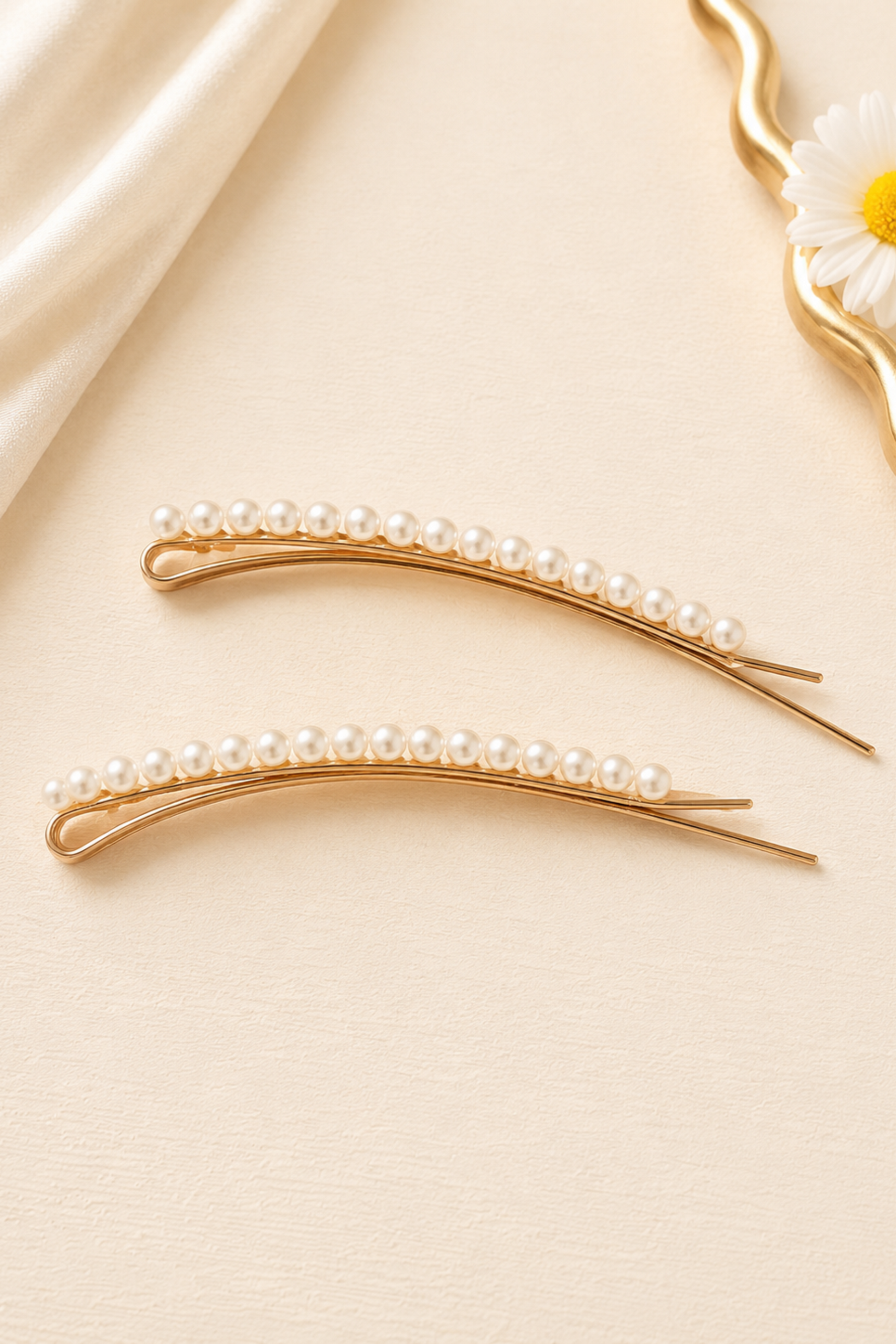 Two gold hairpins with pearls on a beige fabric background