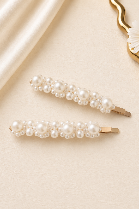Two pearl hair clips on a beige surface with a daisy in the corner.
