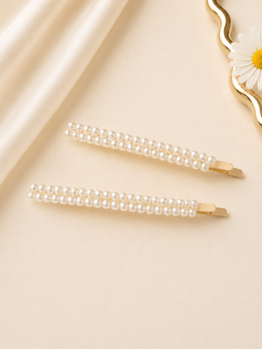 Two pearl hair clips on a beige fabric background with a decorative item in the corner.