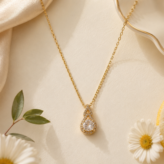 Gold necklace with a diamond pendant on a beige fabric background with flowers and a lemon slice.