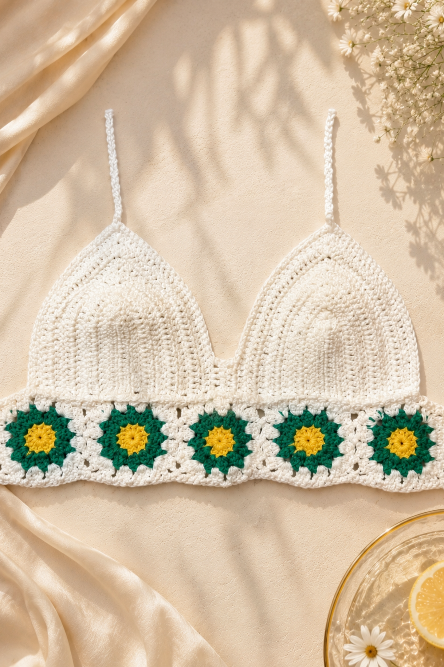 White crochet bikini top with green floral patterns on a beige fabric background