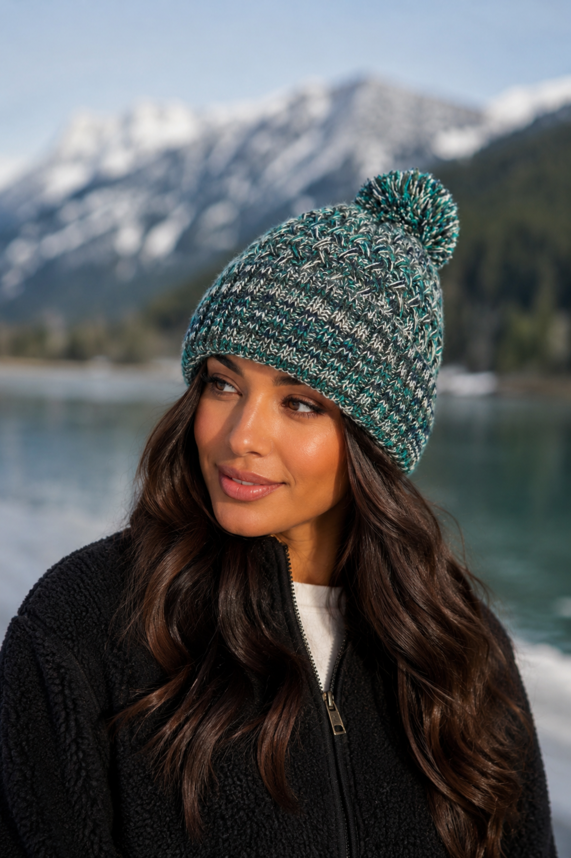 Woman wearing a teal knit beanie with a pom-pom in a mountainous landscape.