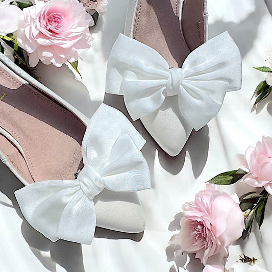 Front view of shoes featuring ivory bow clips attached to the toe, decorative slip-on shoe accessories for women.