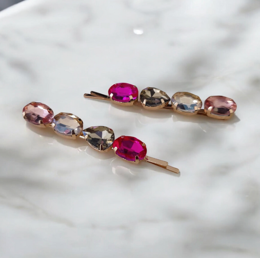 Two hair pins with multicolored gemstones on a white textured surface