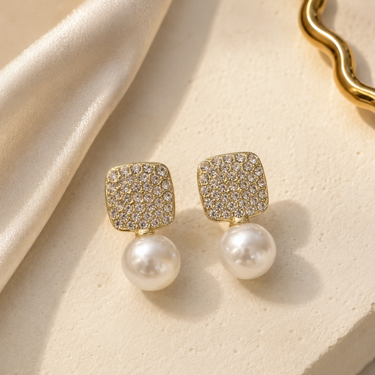 Gold earrings with pearl drops on a beige fabric background