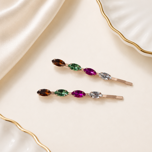 Two hair clips with multicolored gemstones on a beige fabric background