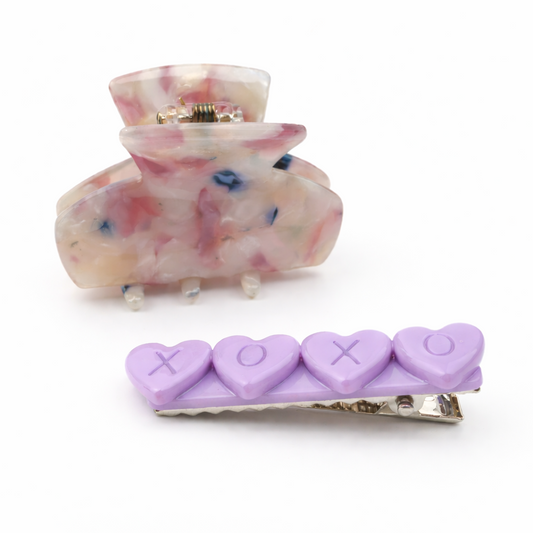 Two hair clips on a white background, one pink with heart designs and the other purple.