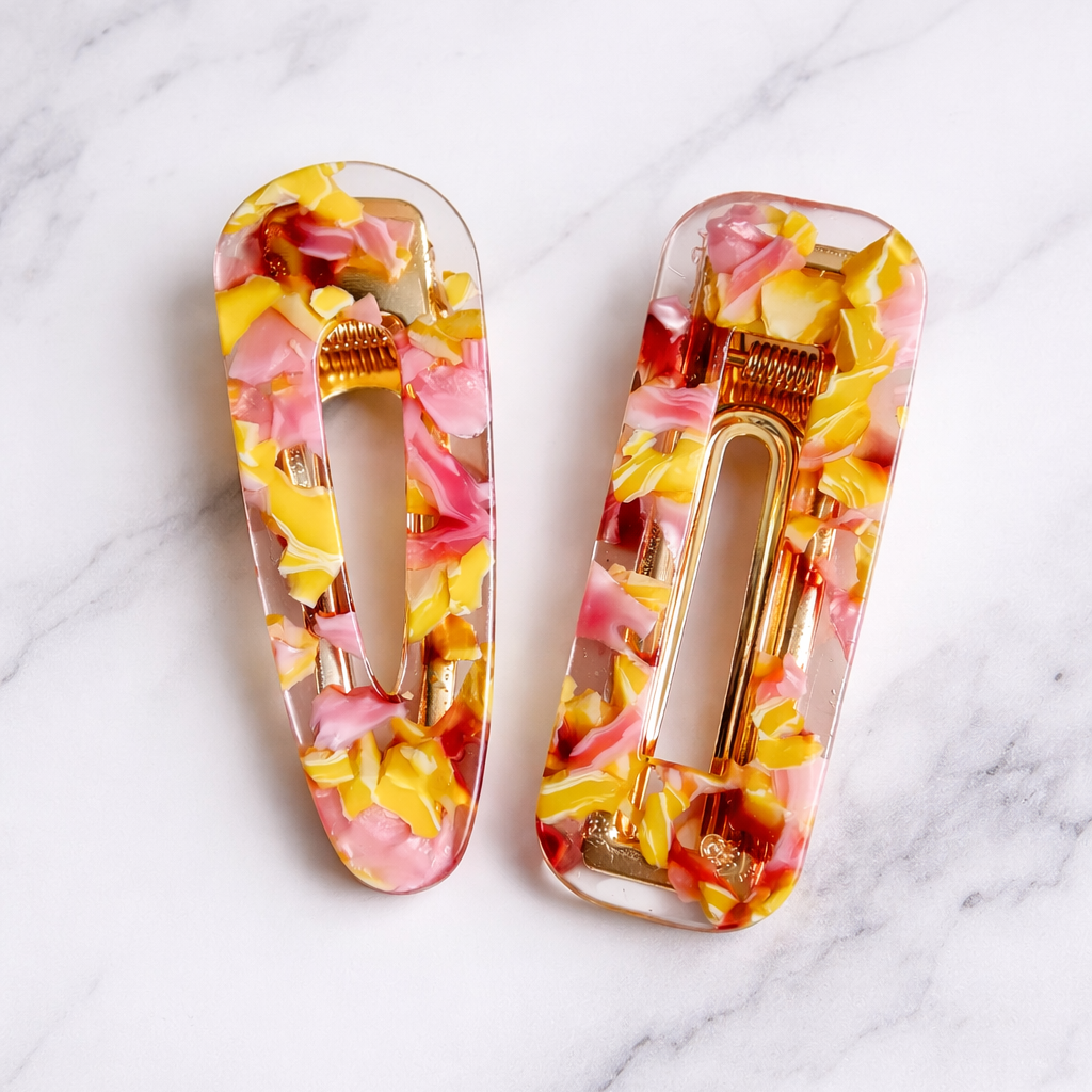 Two yellow and pink hair clips on a marble surface