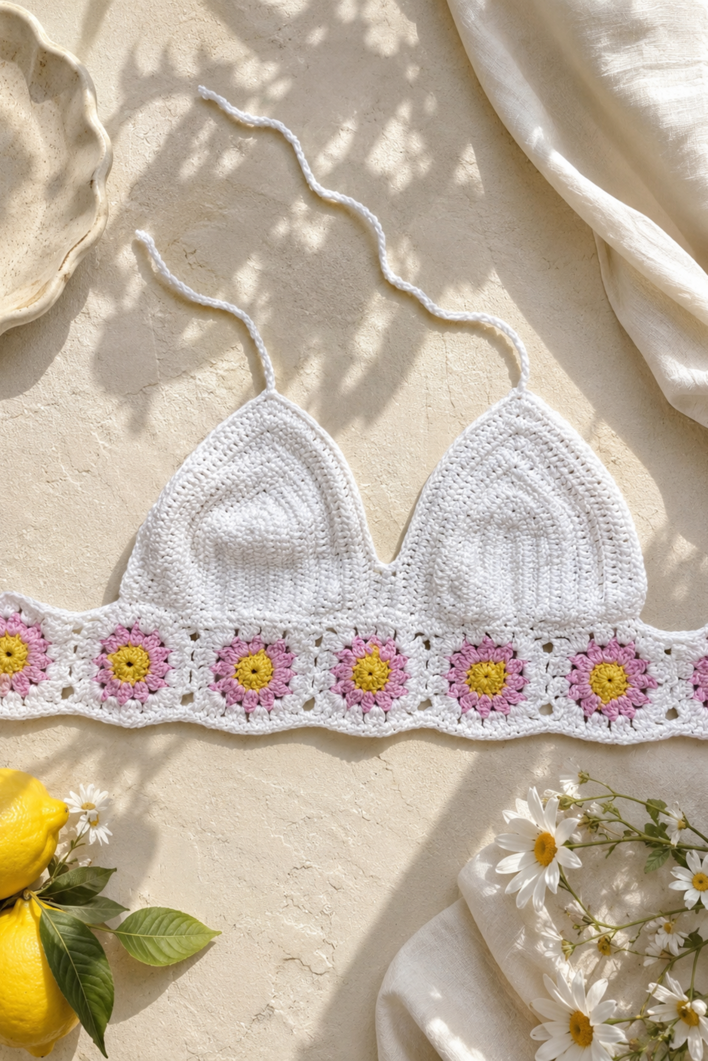 White crochet bikini top with floral patterns on a light background with lemons and flowers.