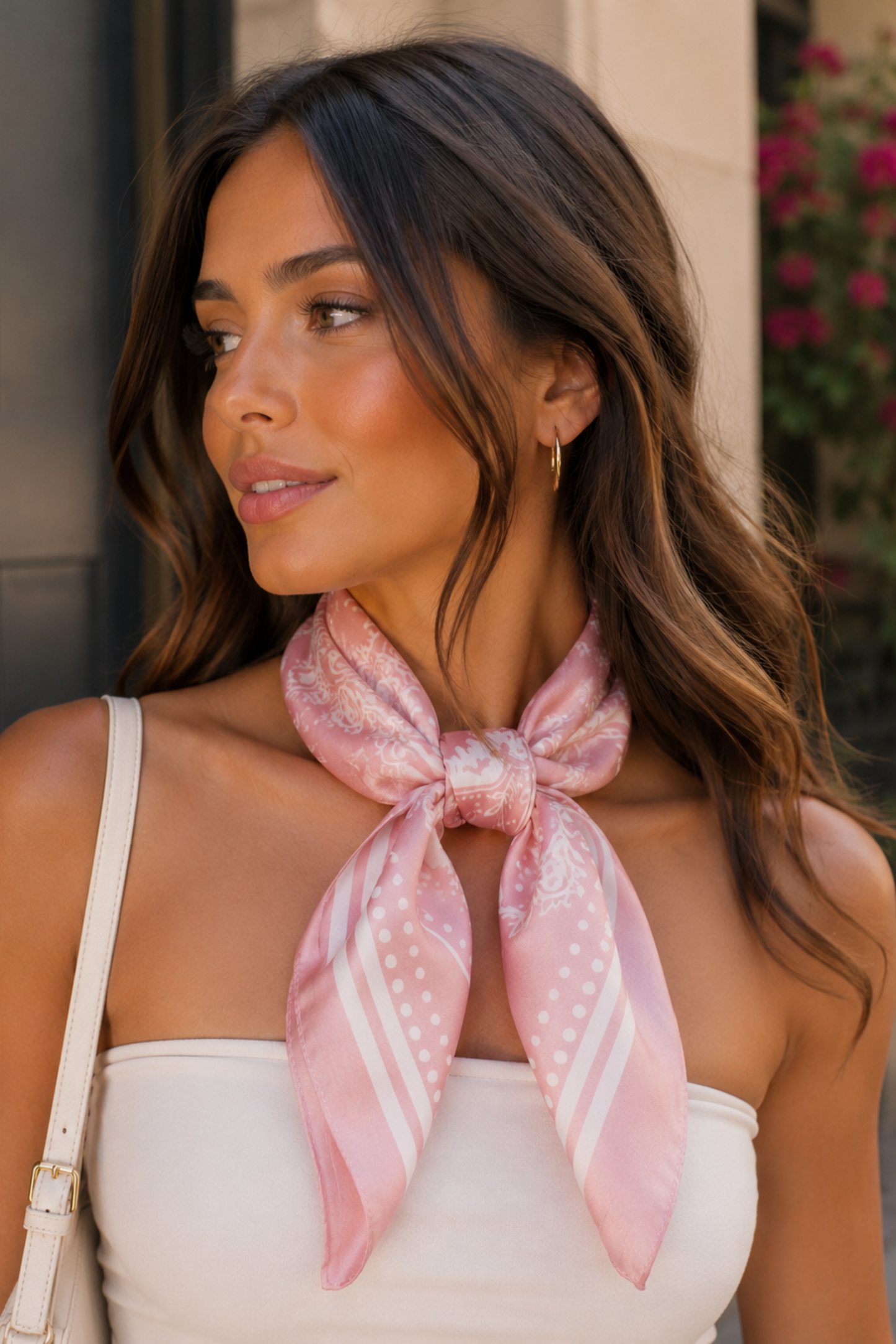 Woman wearing a pink scarf with a pattern, standing outdoors.