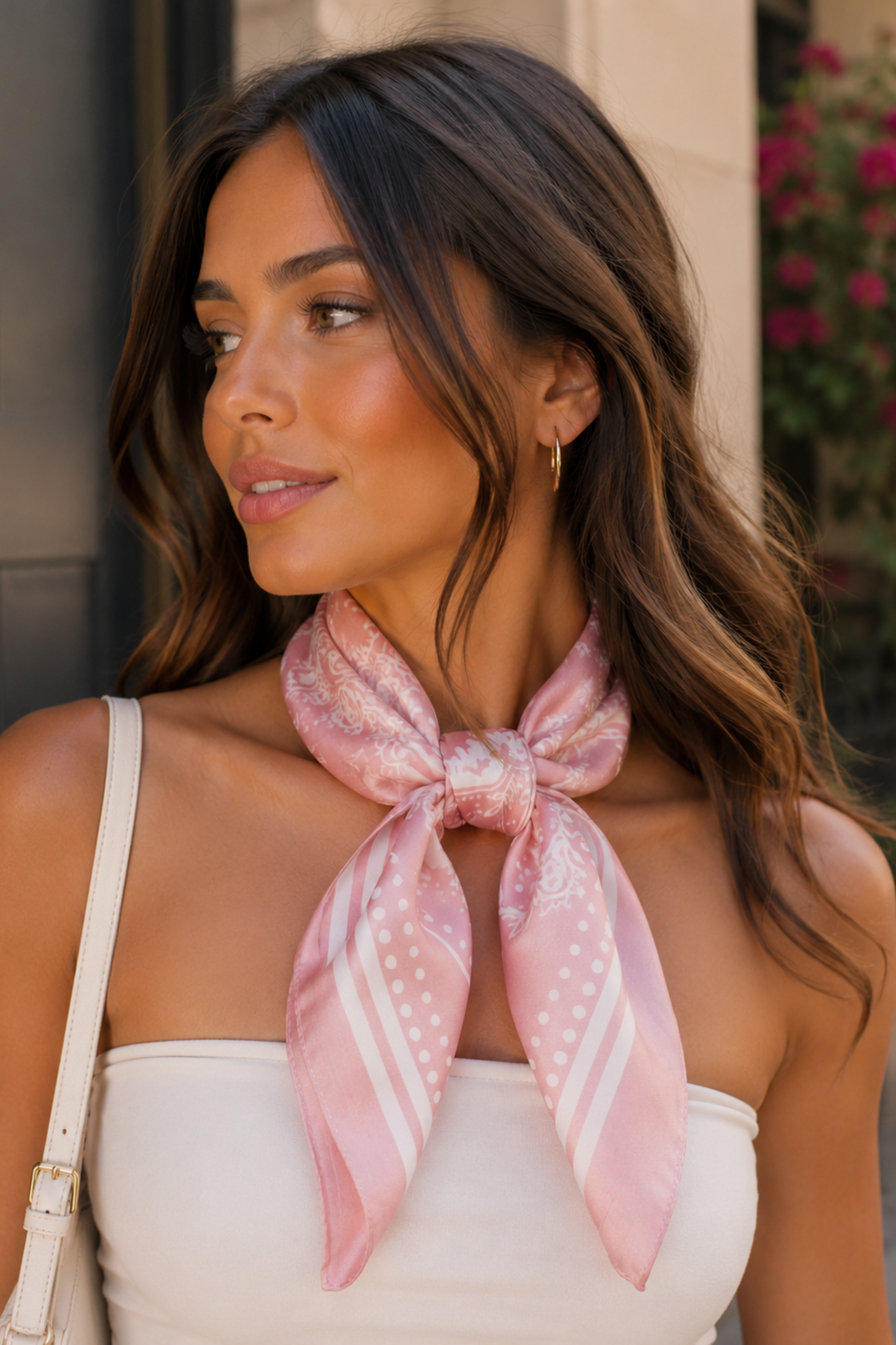 Woman wearing a pink scarf with a pattern, standing outdoors.