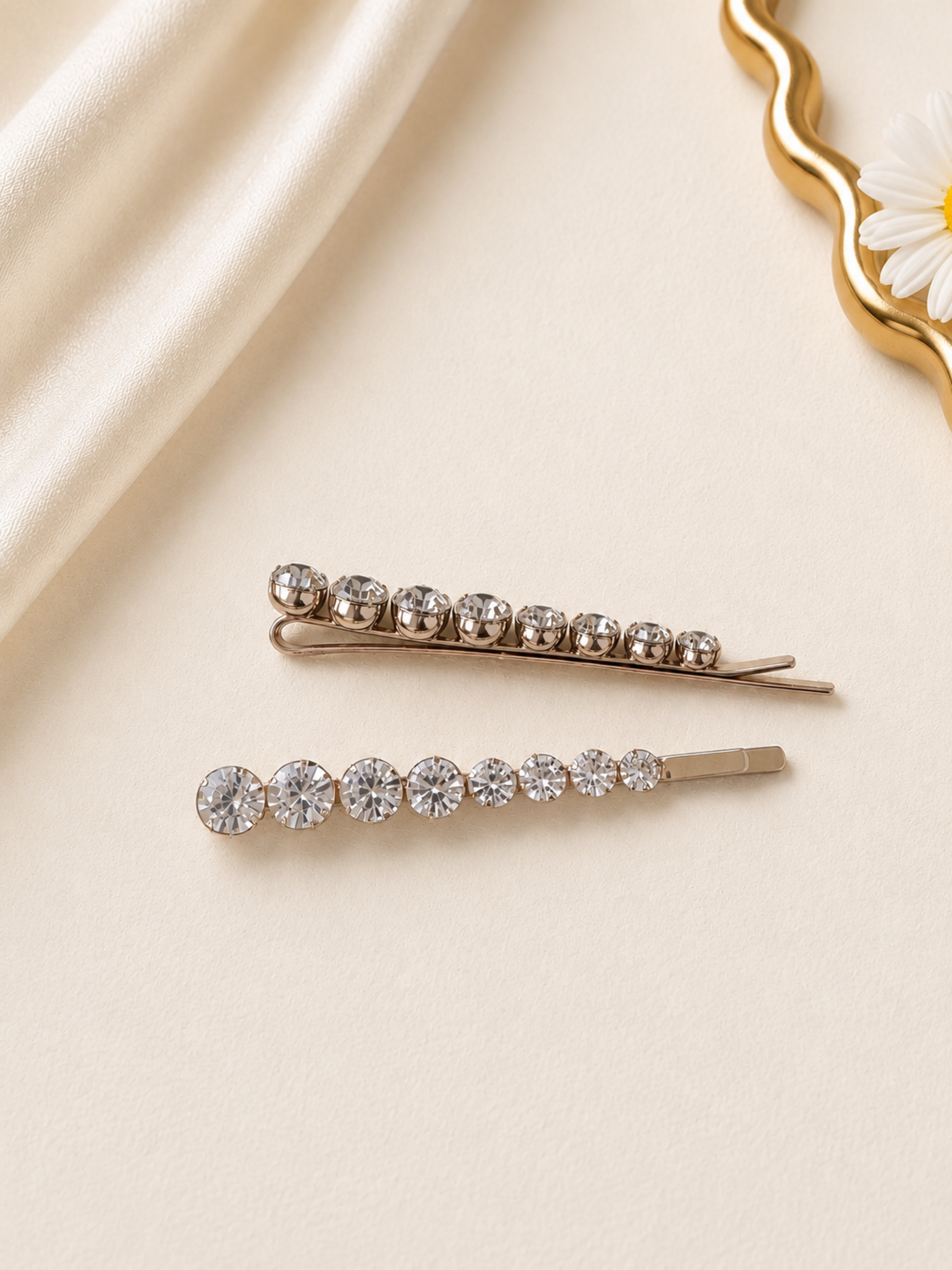 Two gold hair pins with crystal stones on a beige fabric background