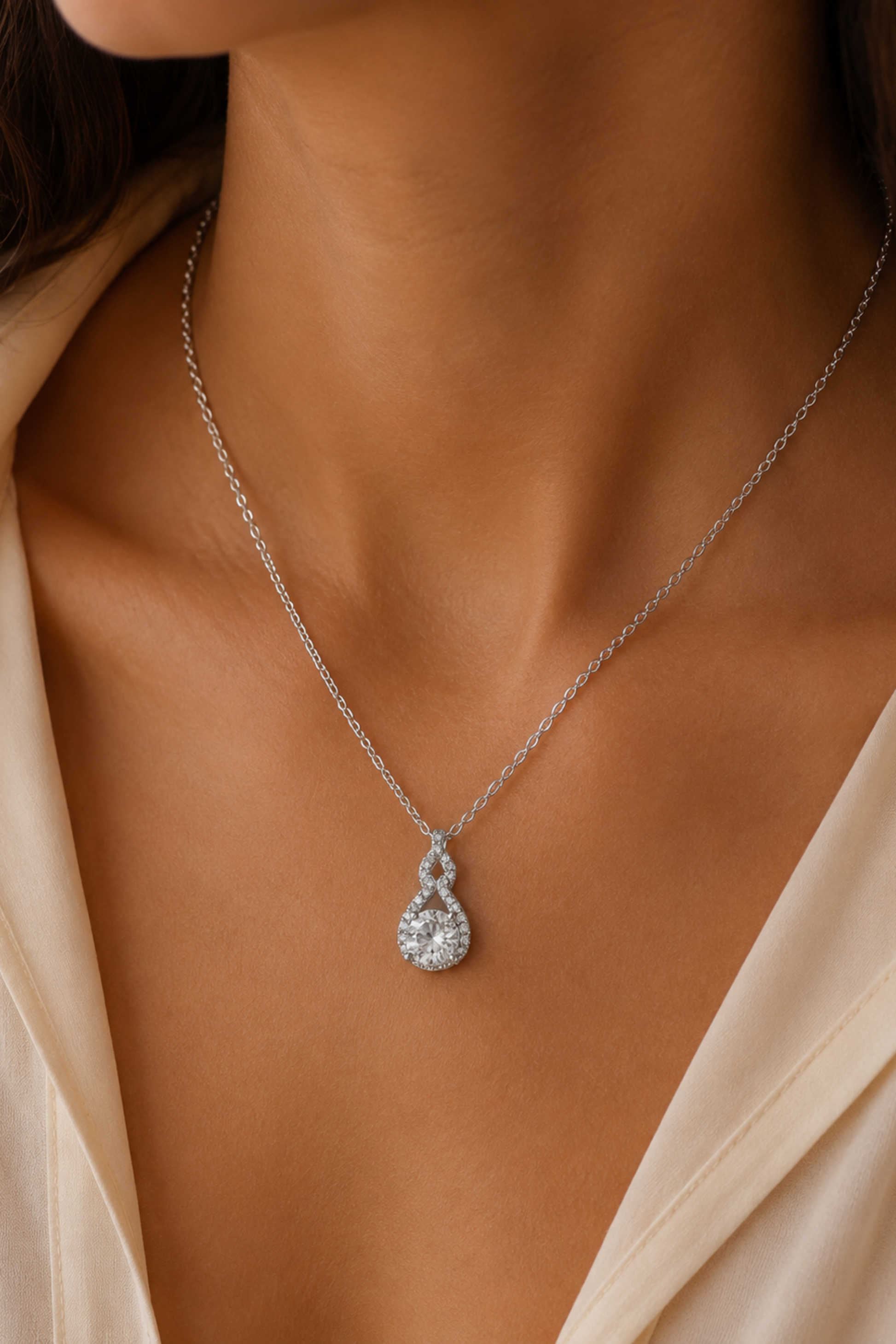 Close-up of a silver necklace with a teardrop-shaped pendant on a person wearing a beige top.