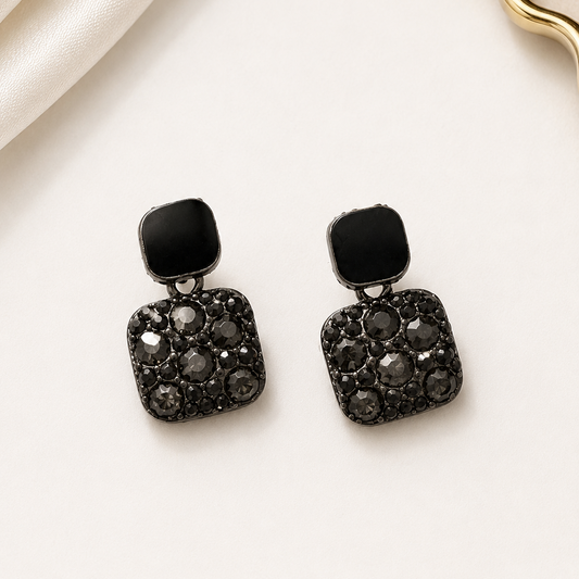 Black square earrings with gemstones on a beige fabric background