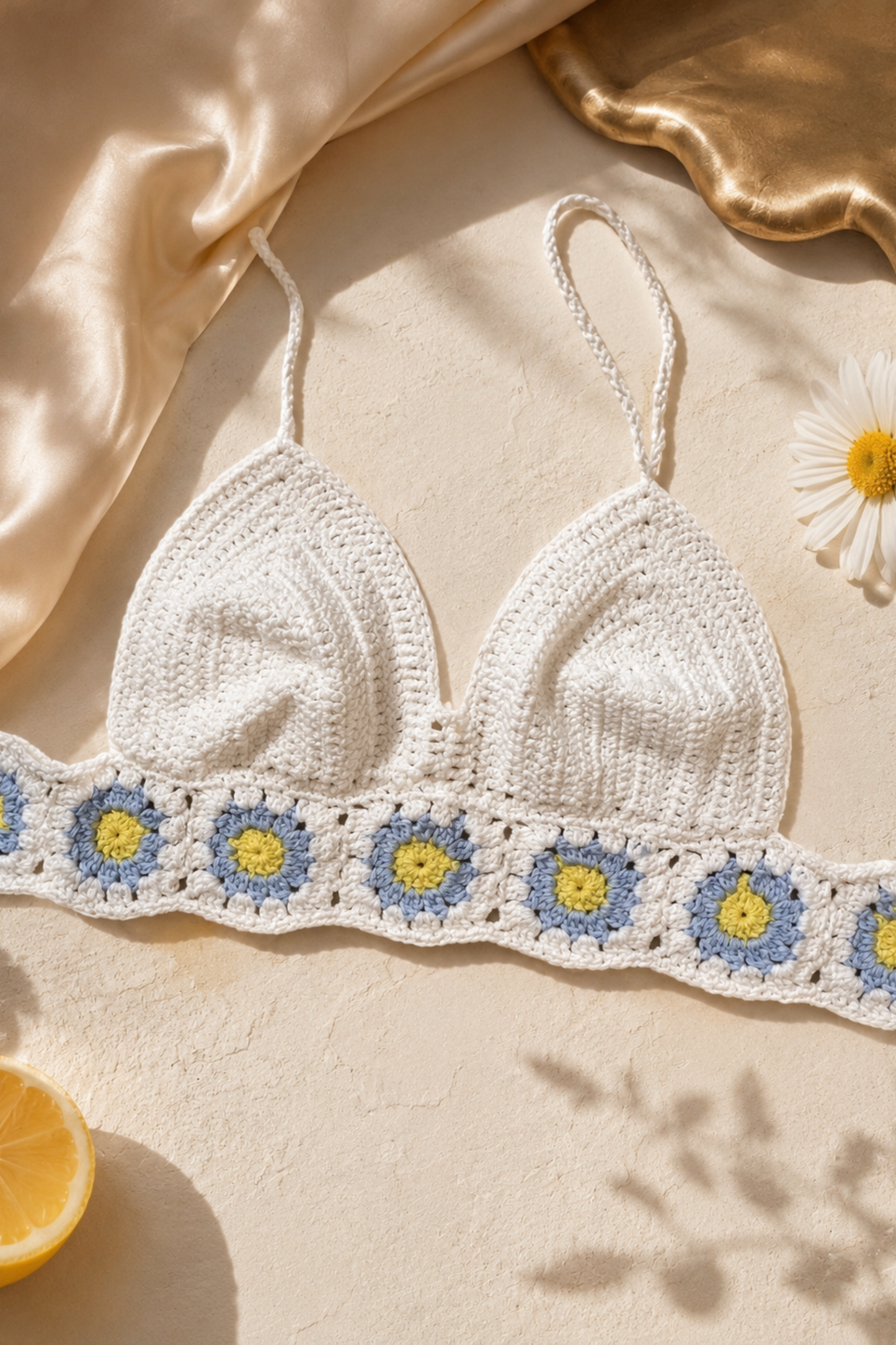 White crochet bikini top with floral details on a beige fabric background